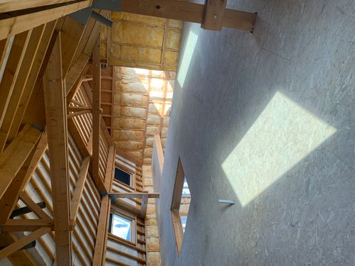 Spacious unfinished attic with exposed wood beams, insulated walls, and sunlight on the floor.