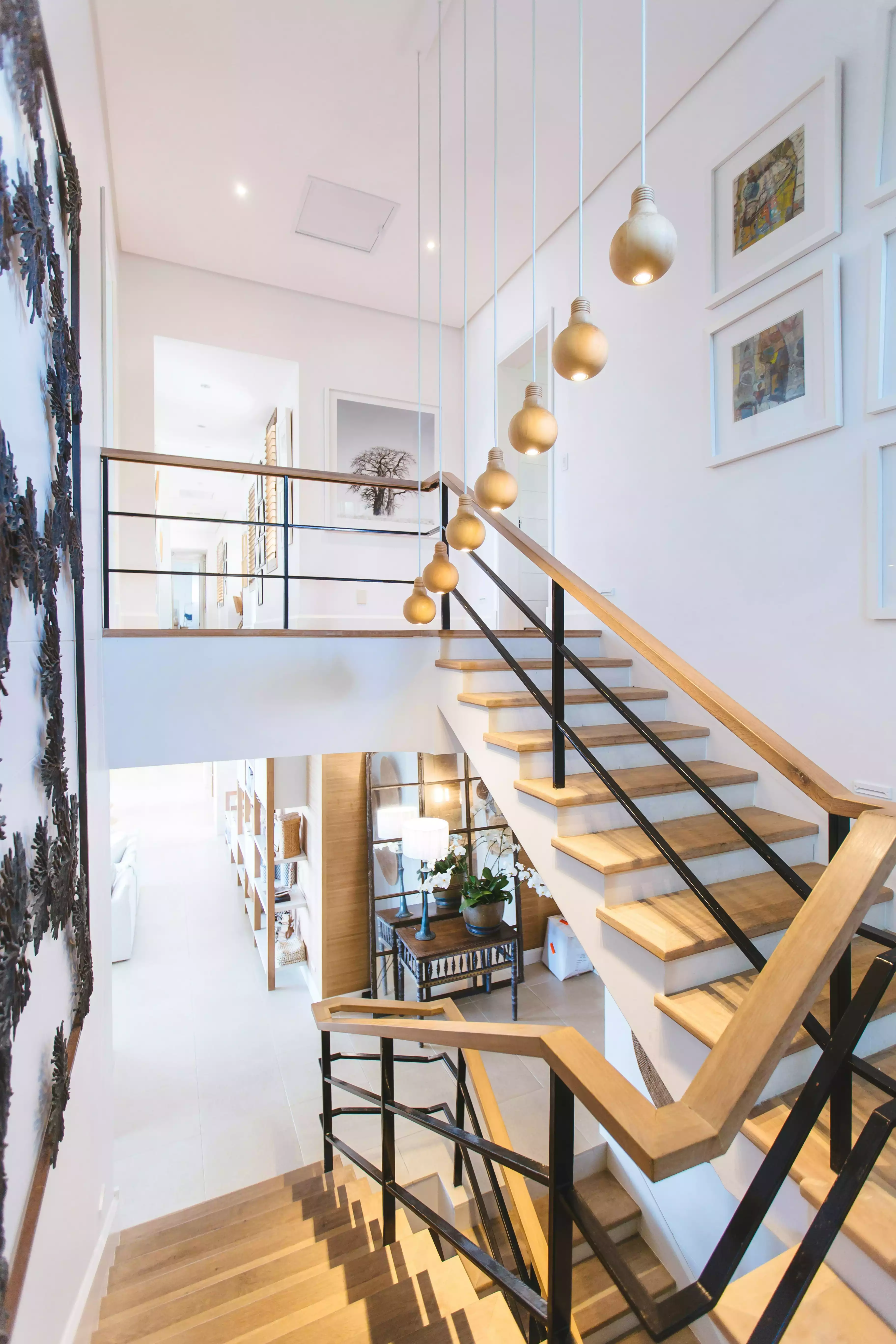 Modern wooden staircase with black railings and hanging bulb pendant lights in a bright home interior.