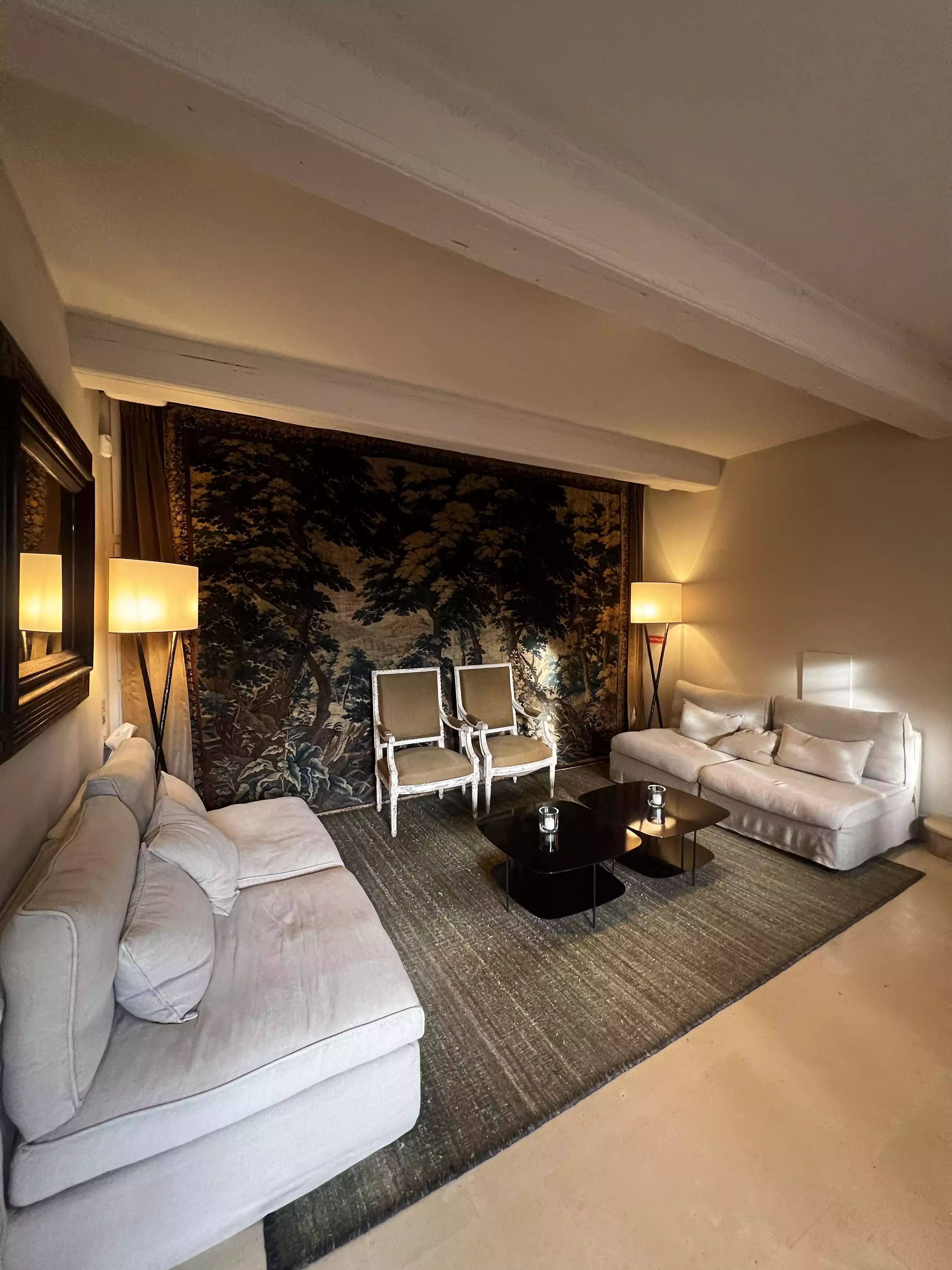 Cozy living room with two white sofas, two chairs, black coffee tables, and patterned wall tapestry.