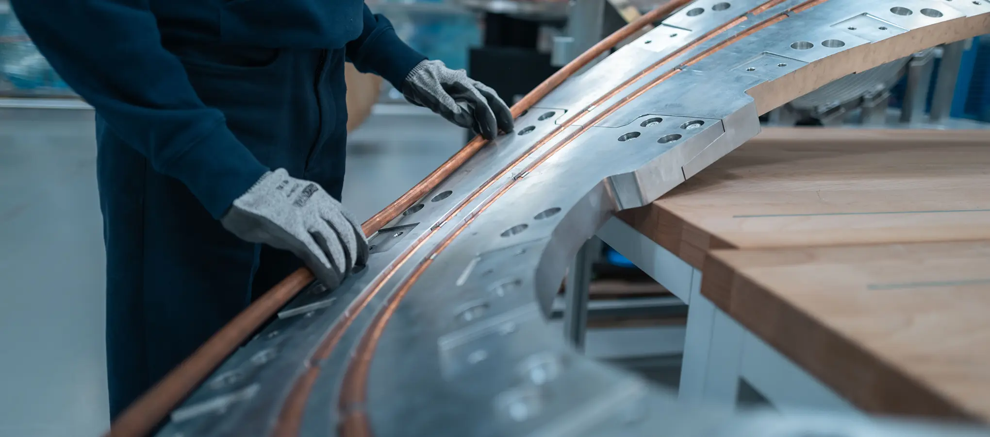 Behandschuhte Hände bearbeiten ein gebogenes Metallbauteil mit eingelassenen Kupferleitern in einer Werkstatt von Proxima Fusion.