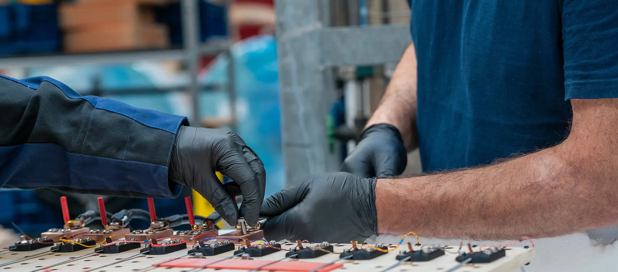 Zwei Mitarbeitende verbinden in der Werkstatt feine Leitungen mit den Kontakten eines technischen Bauteils.