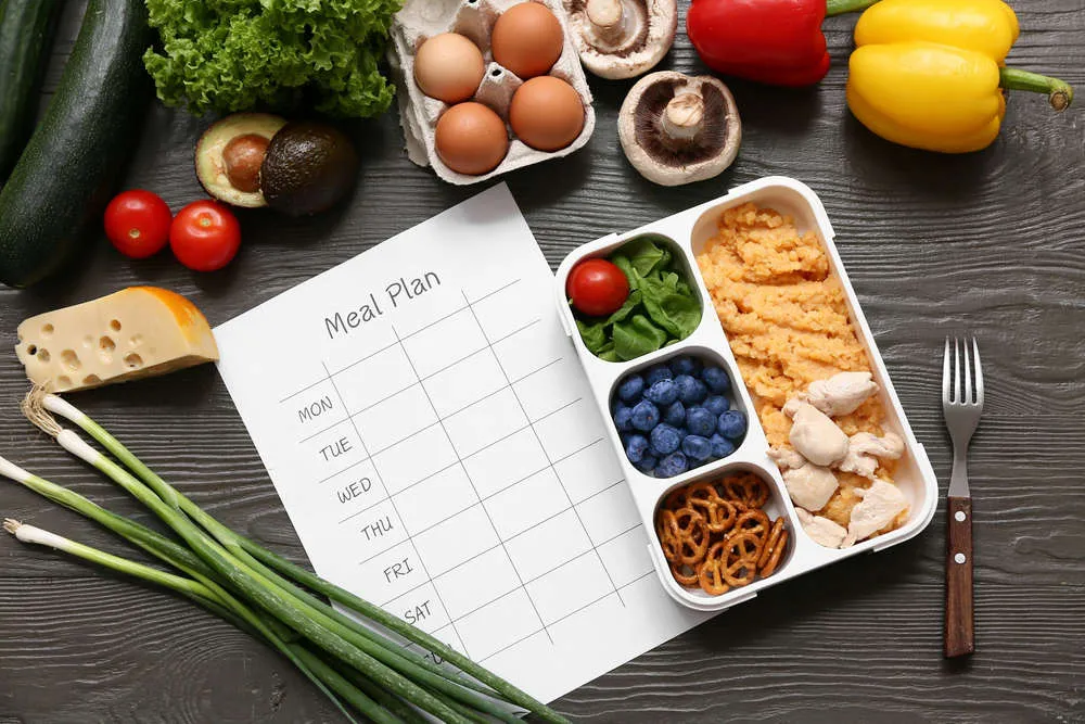 Weekly meal plan beside a packed lunch box and fresh ingredients
