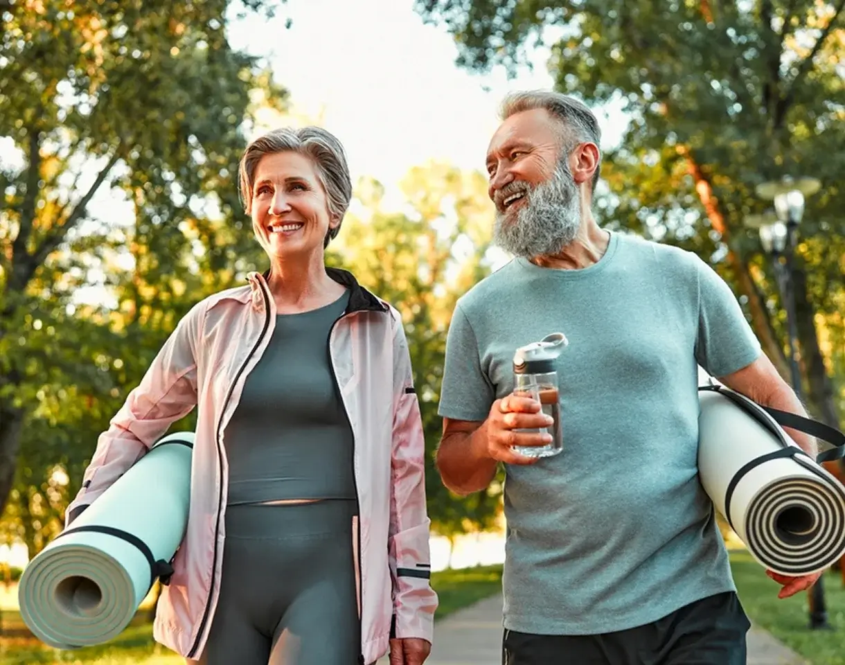 Active older couple carrying yoga mats and water outdoors