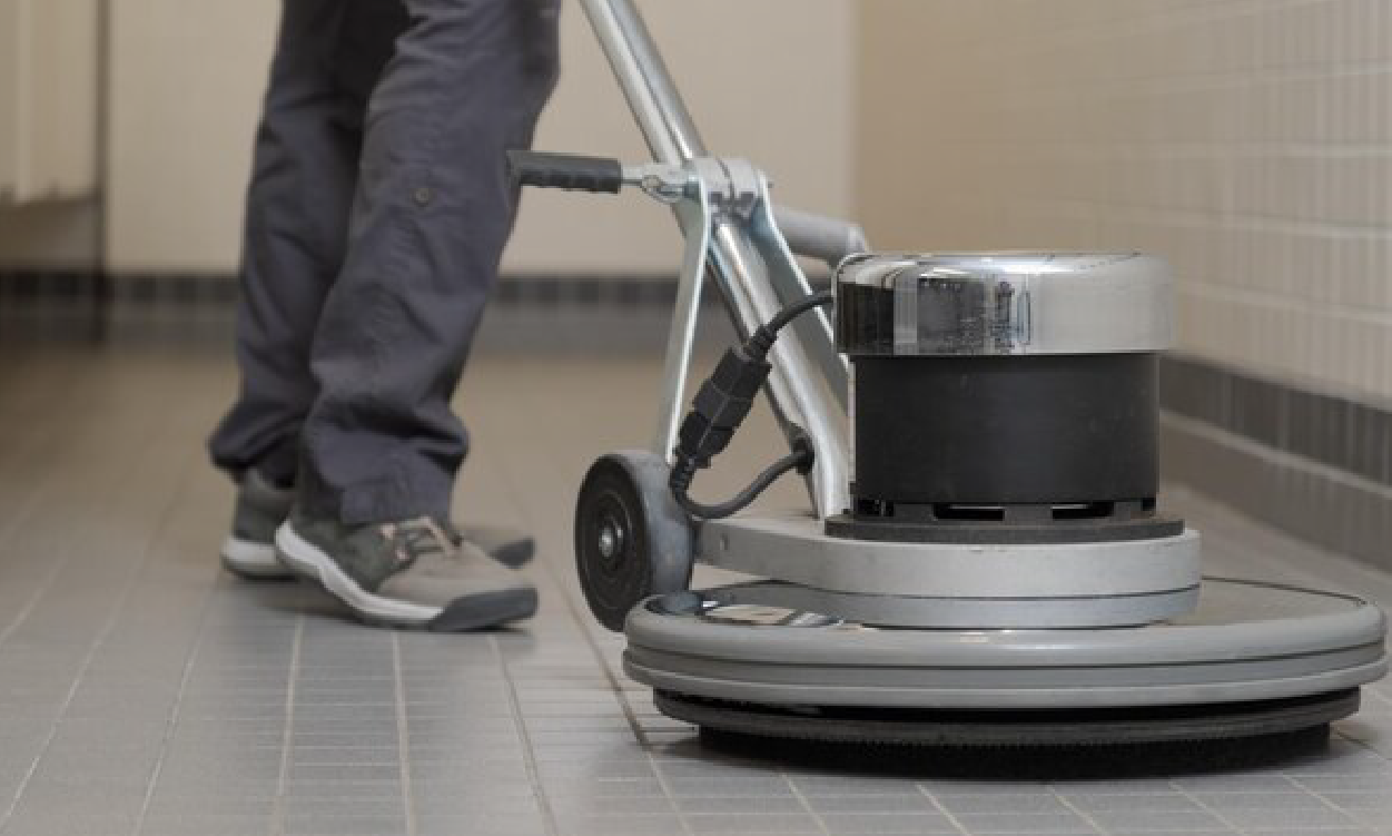 Person wearing gray pants and gray shoes operating a professional floor cleaning machine on a tiled floor.