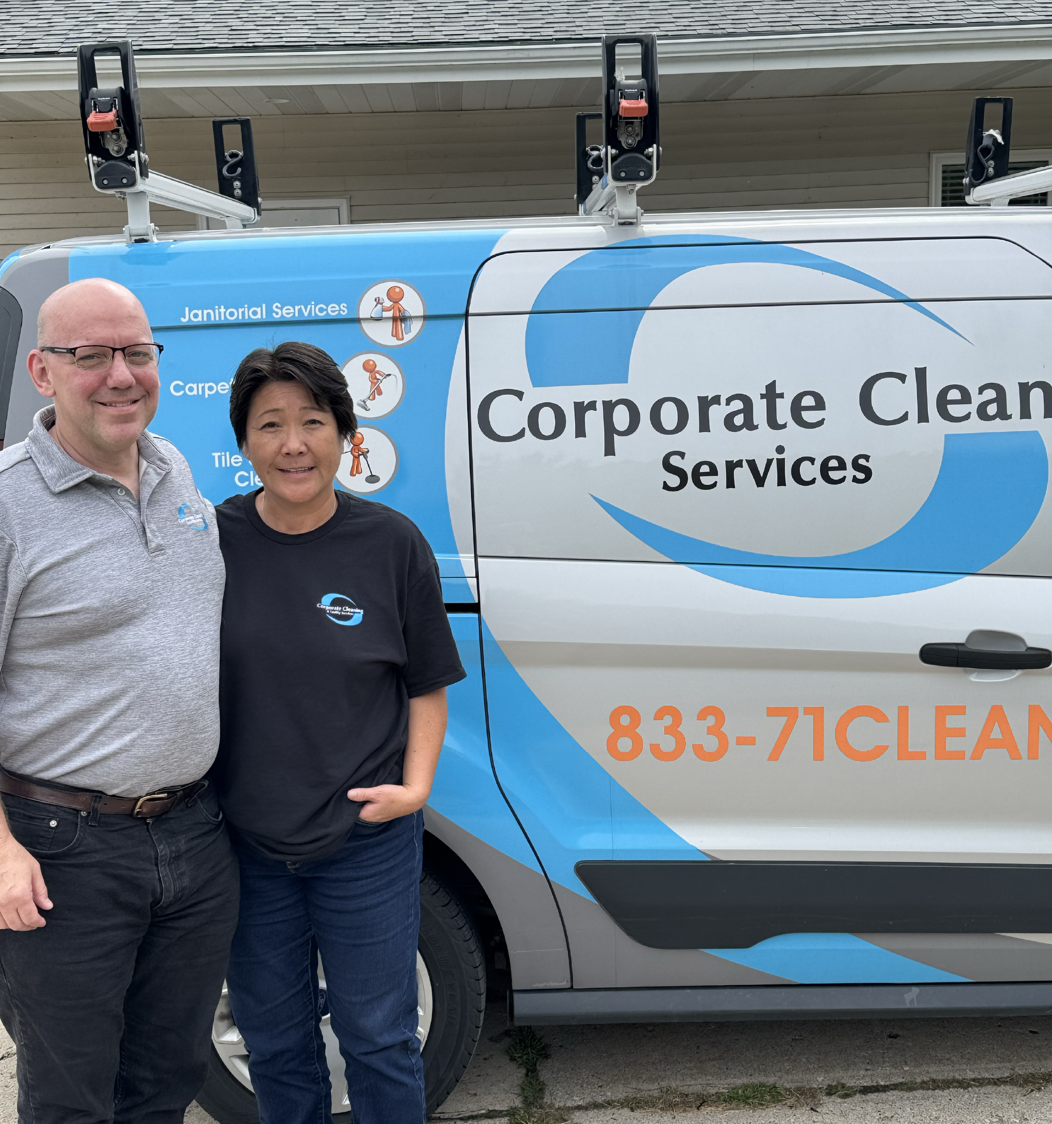 A man and a woman standing in front of a Corporate Cleaners Services van, both smiling and wearing branded shirts. The van displays cleaning services including Janitorial Services, Carpet Cleaning, and Tile Cleaning with icons.