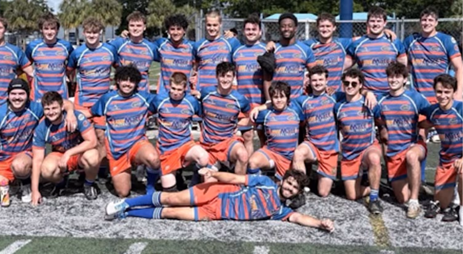 Group photo of young rugby players in striped blue and orange uniforms on a field.