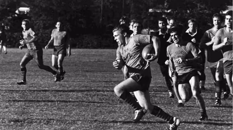 Black and white photo of a football player running with the ball while others chase him on a field.
