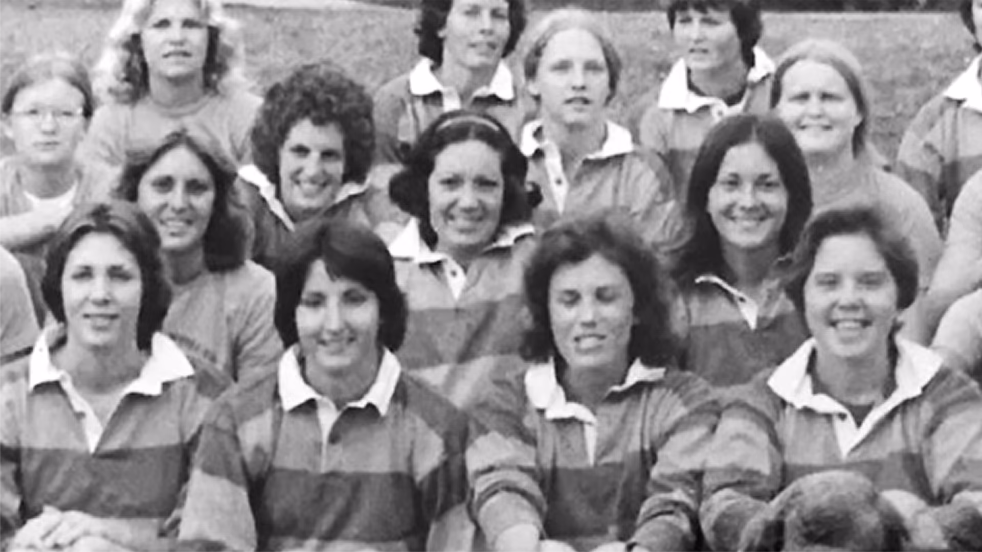 Black and white photo of women in striped rugby shirts posed closely together, some smiling, in an outdoor setting.