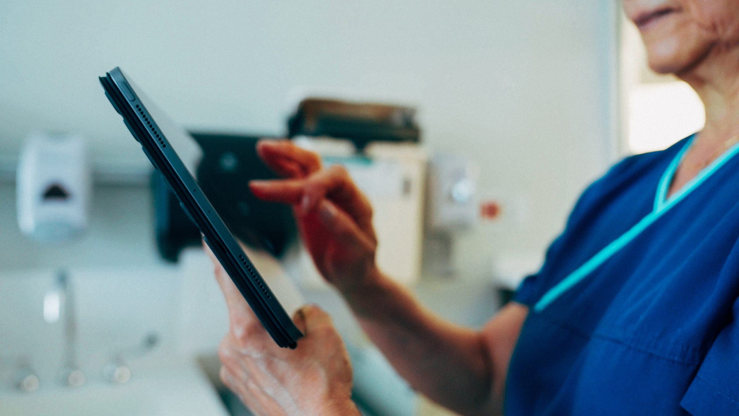 Healthcare worker in blue scrubs using a tablet device in a clinical setting.