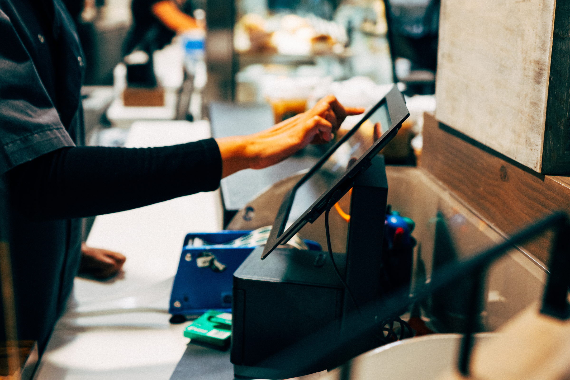 Person using a touchscreen point-of-sale system at a cafe counter.