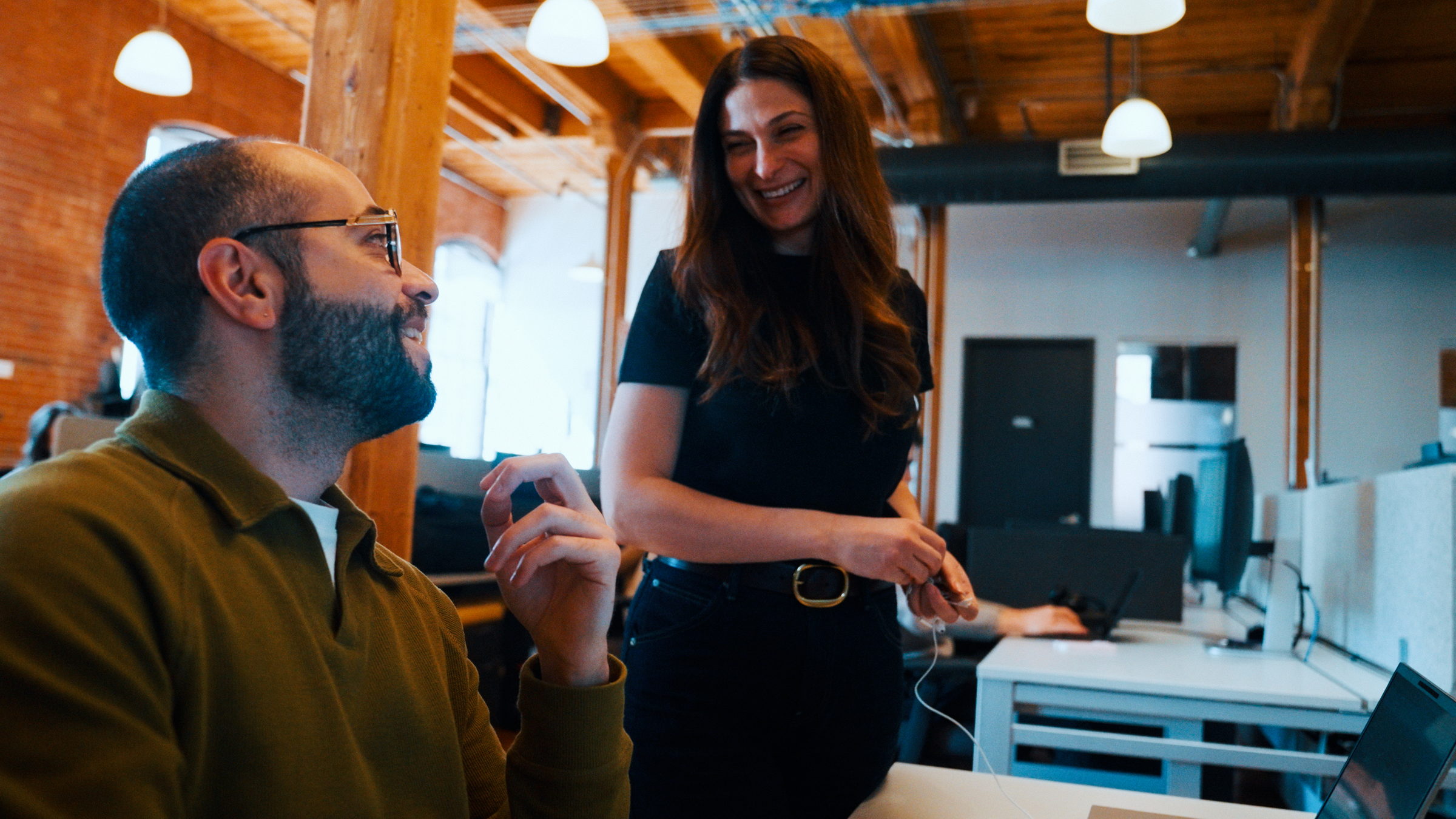 Man and woman smiling and talking together in a modern office with wooden beams and desks.
