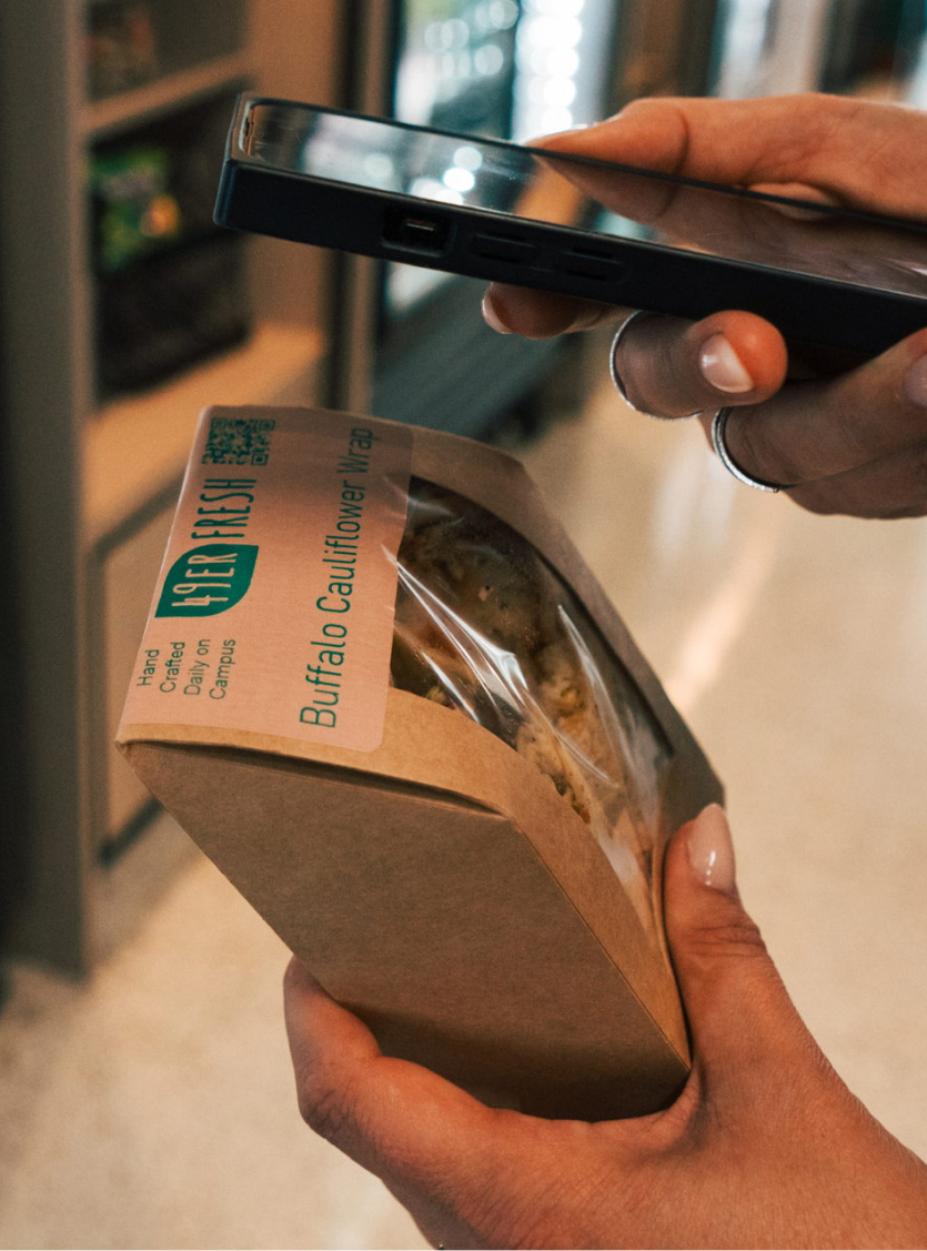 Person scanning breakfast sandwich labeled Buffalo Cauliflower Wrap with a smartphone.