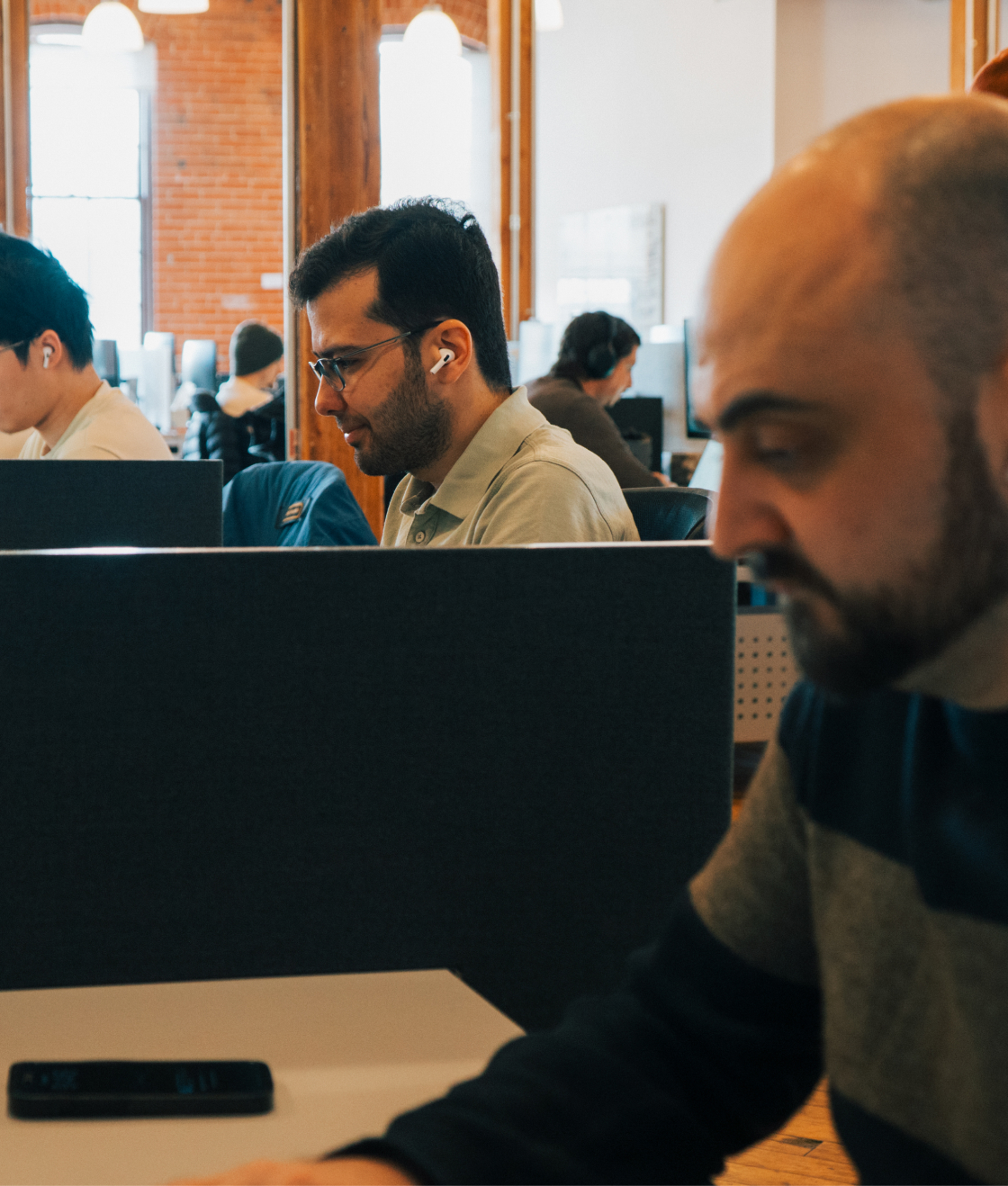 People working at desks in a modern office with wooden beams and brick walls.