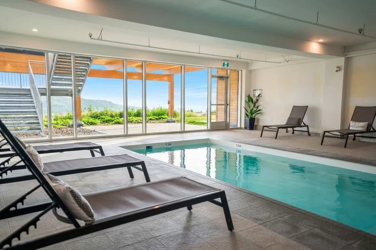 Piscine intérieure d'Aurea Charlevoix avec mur vitré ouvrant sur les montagnes et plafond de bois, chaises longues en bordure