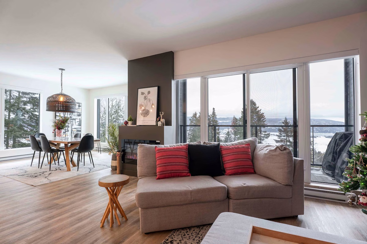 Séjour du condo 211 avec fenestration pleine hauteur sur le fleuve, foyer et coin salon, Aurea Charlevoix