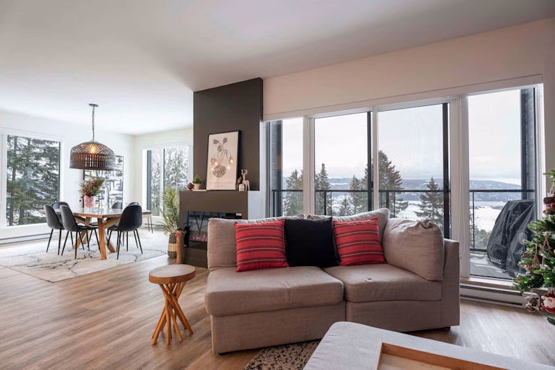 Séjour du condo 211 avec fenestration pleine hauteur sur le fleuve, foyer et coin salon, Aurea Charlevoix