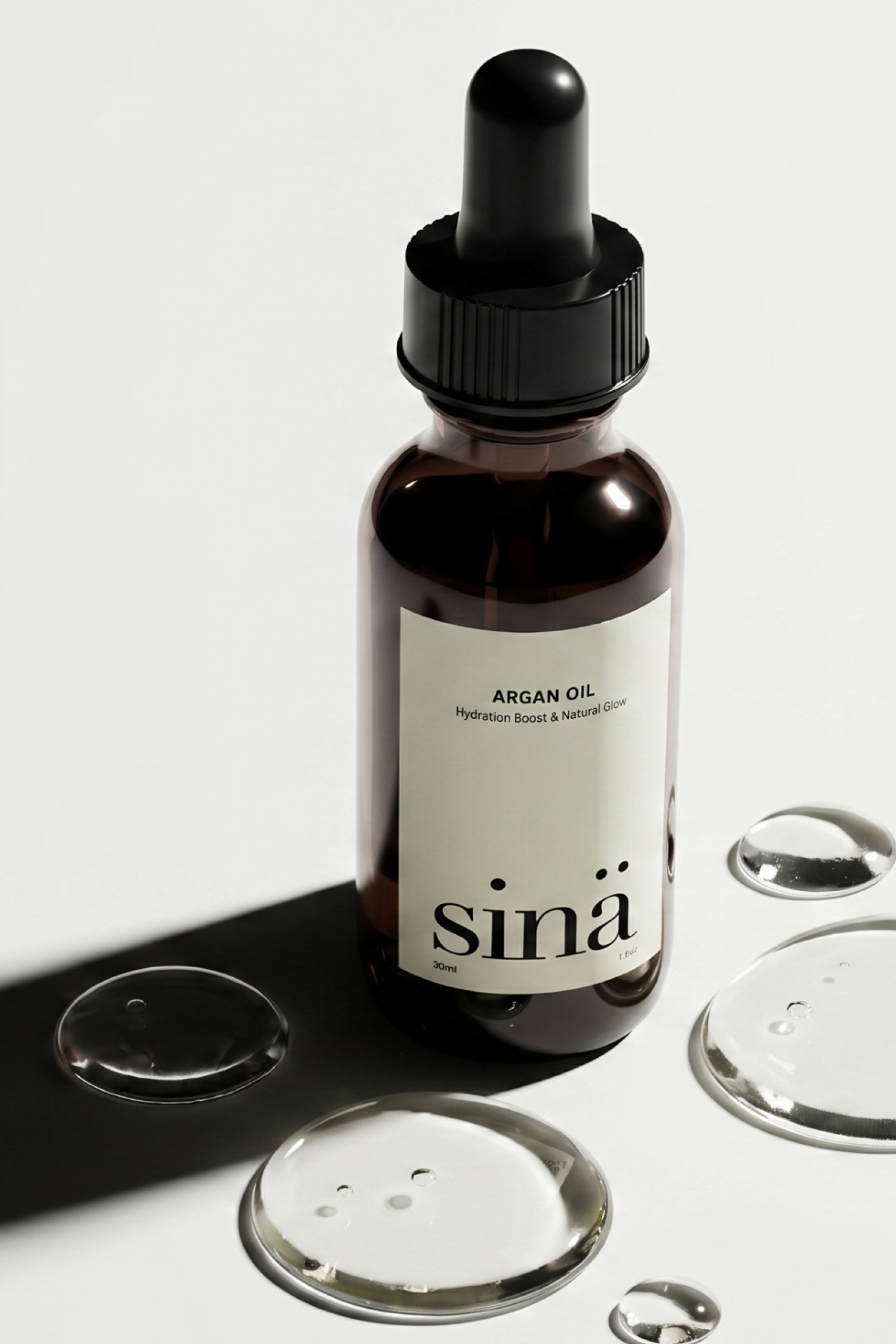 Brown glass dropper bottle labeled 'Argan Oil' with text 'Hydration Boost & Natural Glow' and brand name 'sinä', surrounded by clear liquid droplets on a white surface.