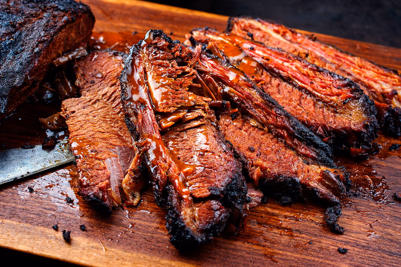 Sliced smoked brisket with a dark crust on a wooden cutting board with juices.