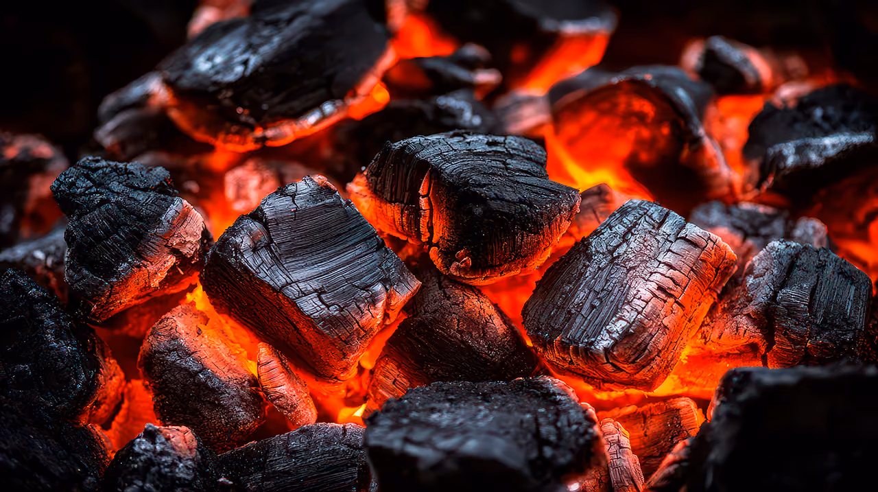Close-up of glowing red hot charcoal pieces with textured black surfaces.