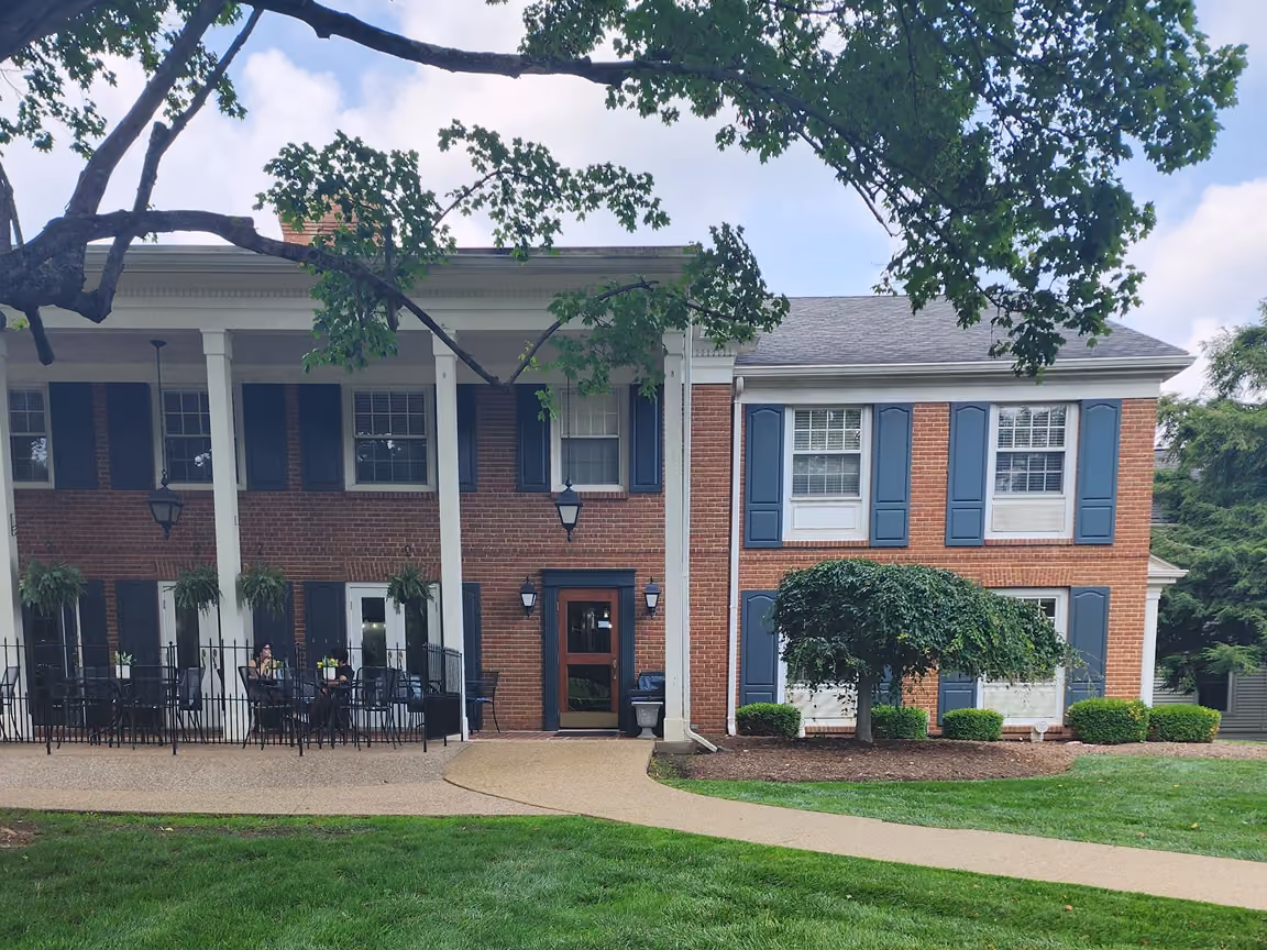 Kenyon Inn & Restaurant with brick exterior and white columns, blue shutters, outdoor seating, and a curved walkway through green lawn.