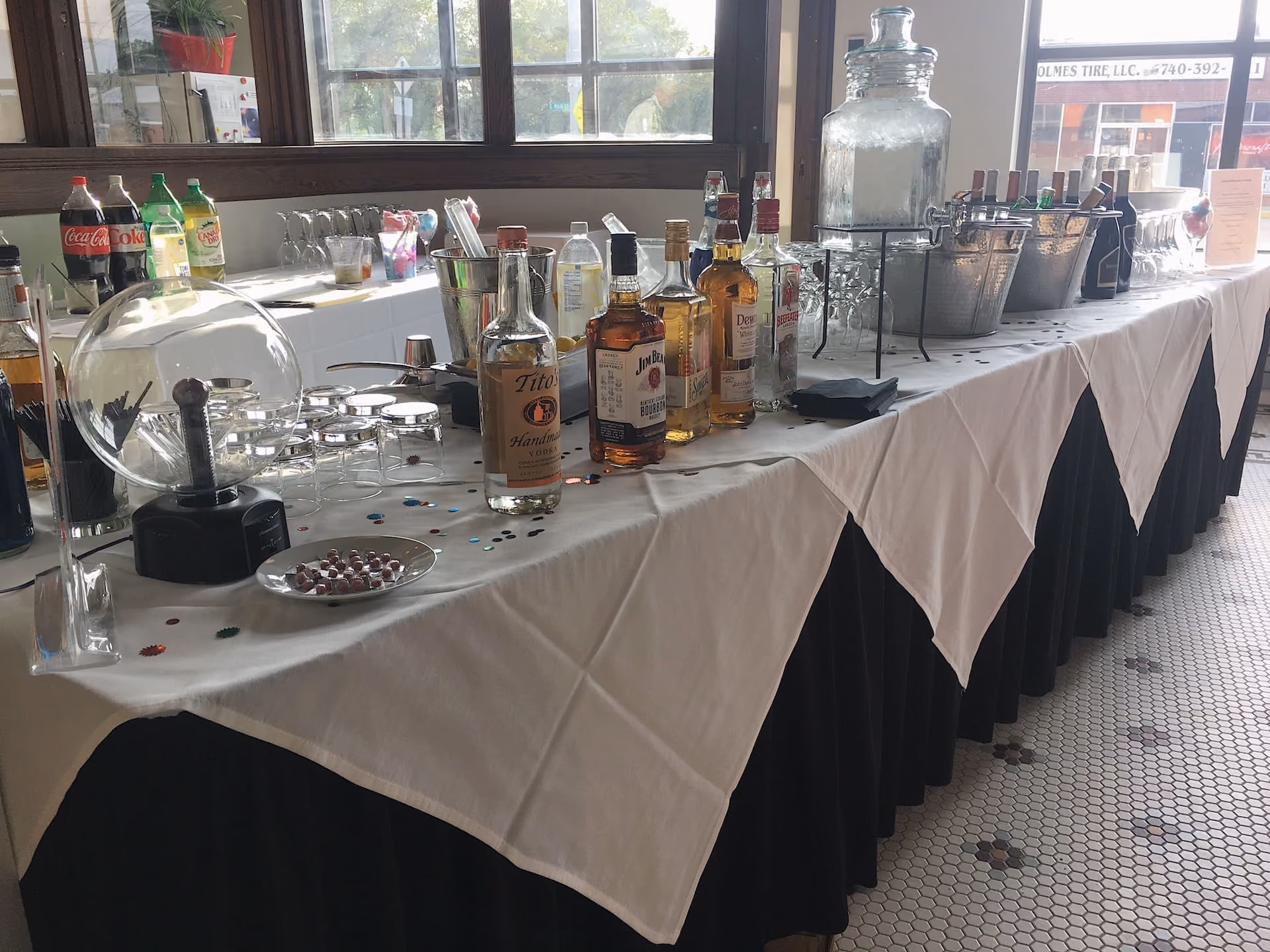 Full service bar set up with liquor bottles, drink glasses, soda, ice dispenser, and cocktail supplies.