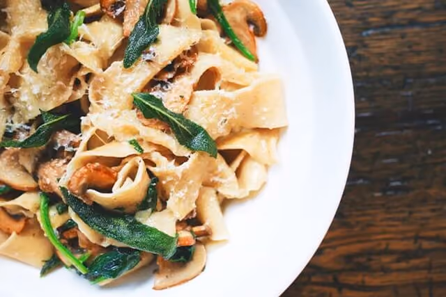 Plate of pasta with sautéed mushrooms and fresh green herbs on a wooden table.