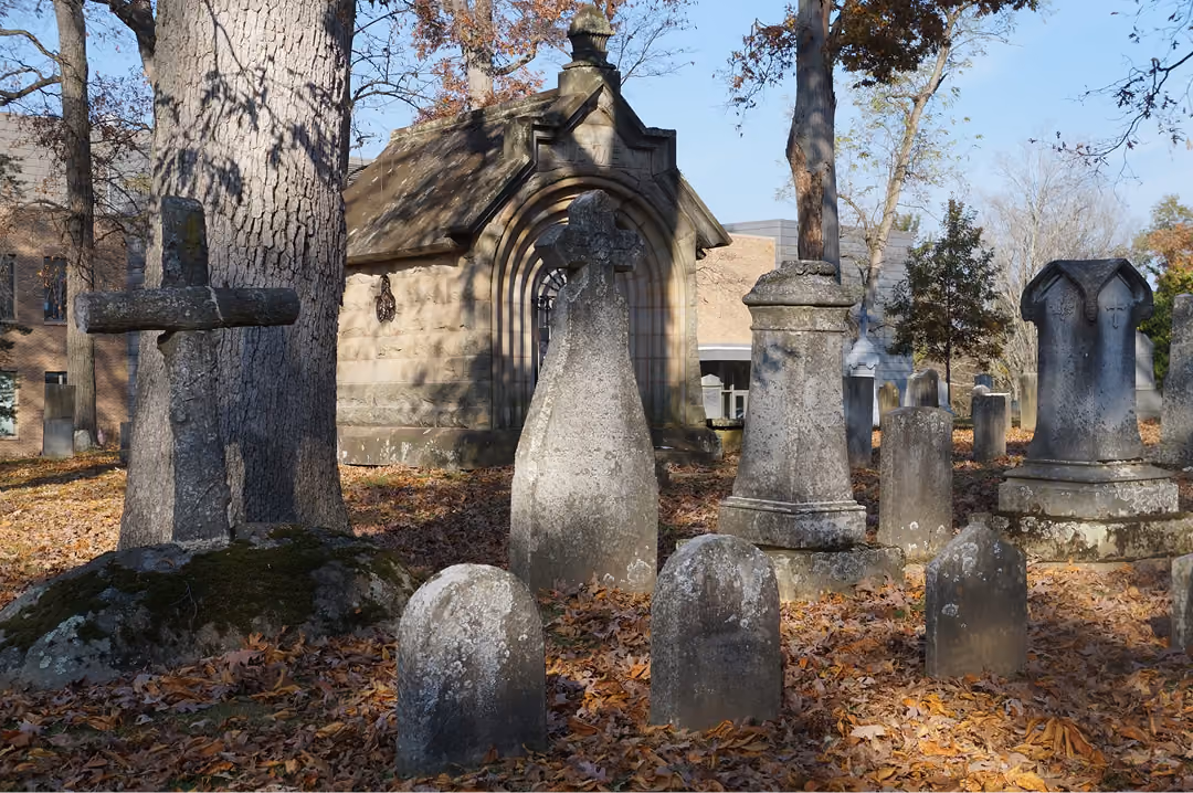 Old gravestones and a mausoleum in a cemetery covered with fallen autumn leaves.