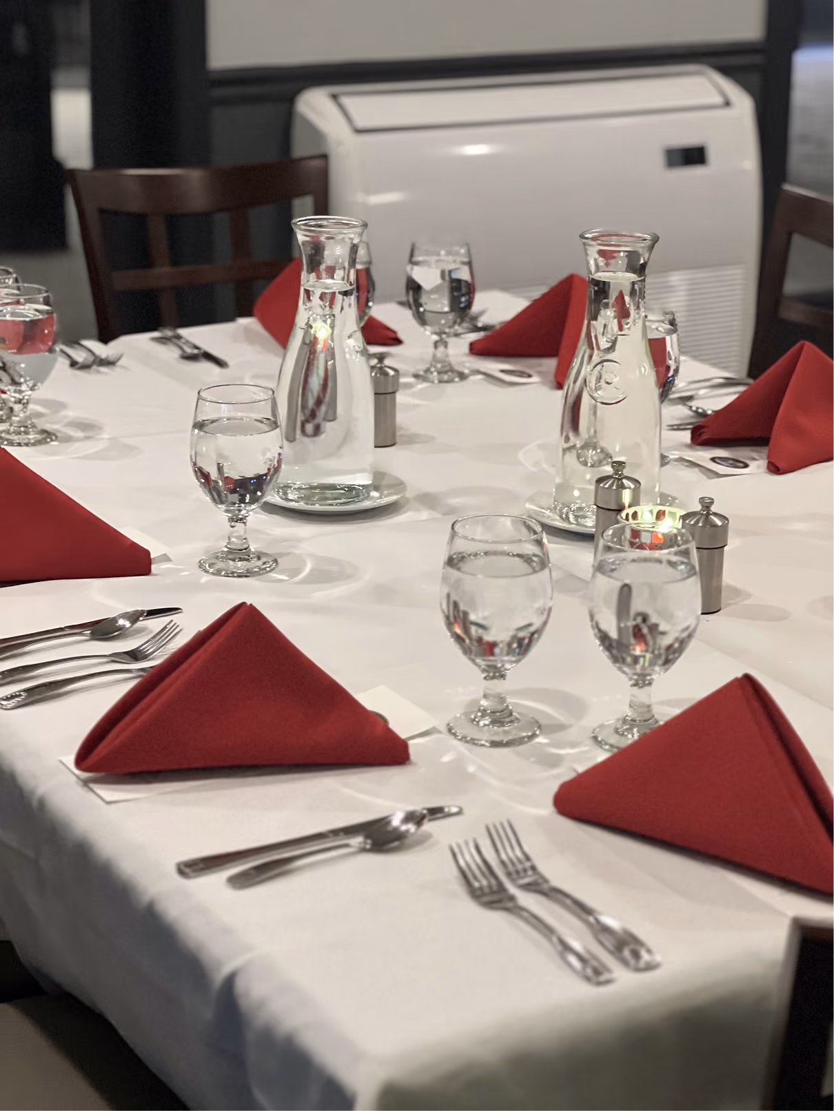 Round restaurant table set with red folded napkins, water glasses, silverware, and water carafes.