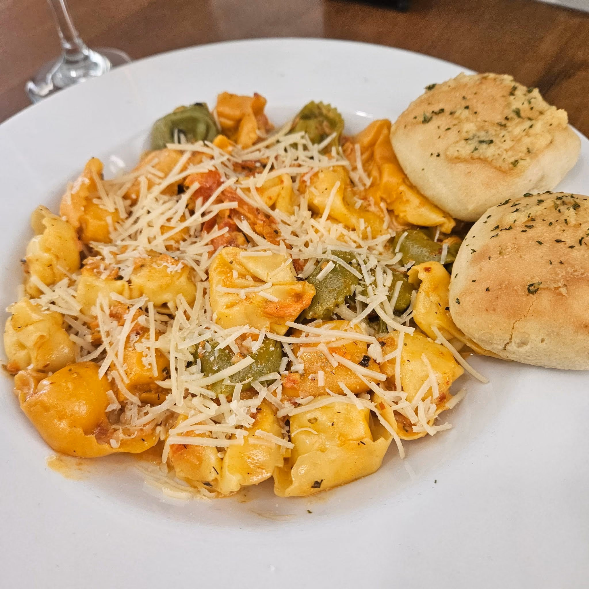 Plate of tri-colored stuffed pasta with tomato sauce and cheese served with two garlic bread rolls.