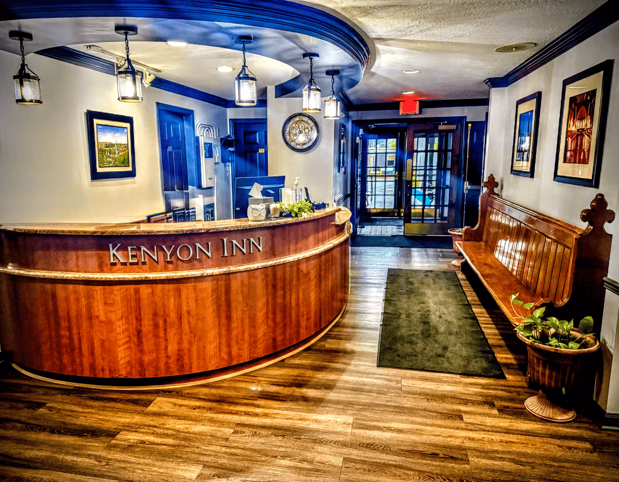 Kenyon Inn front desk with curved wood counter, hanging lights, wooden bench, plant, and exit doors.