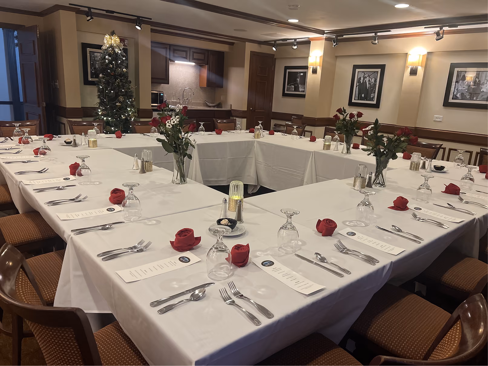U-shaped dining table with white tablecloths, red napkins, floral centerpieces, and place settings in a private room.