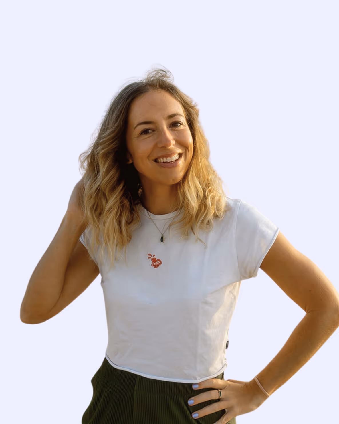 Smiling woman with wavy blonde hair wearing a white cropped t-shirt and green pants posing with one hand on her hip.