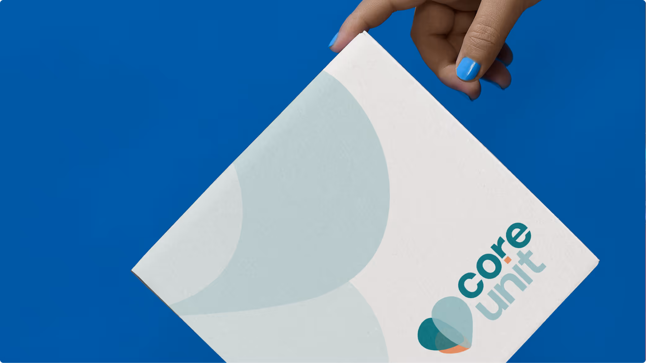 Hand with blue nail polish holding a white box with the Core Unit logo on a blue background.
