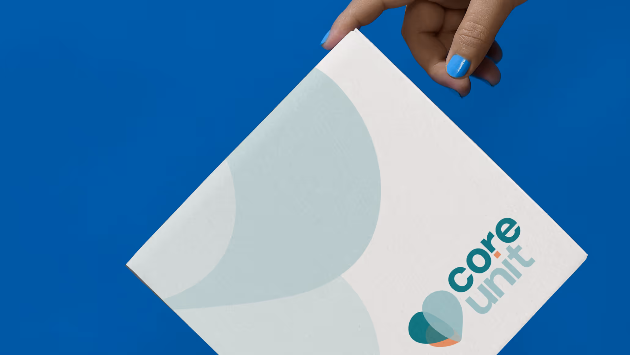 Hand with blue nail polish holding a box with Core Unit logo on a blue background.