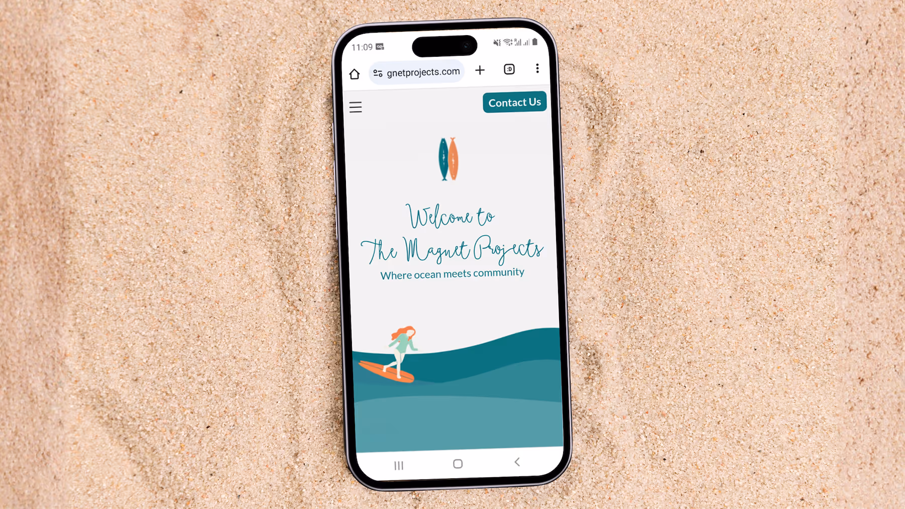 Smartphone on sand displaying a website with the text Welcome to The Magnet Projects and a graphic of a person surfing on stylized ocean waves.