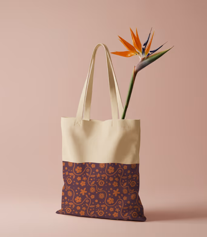 Cream and dark purple tote bag with orange floral pattern at bottom holding a vibrant orange and blue bird of paradise flower.