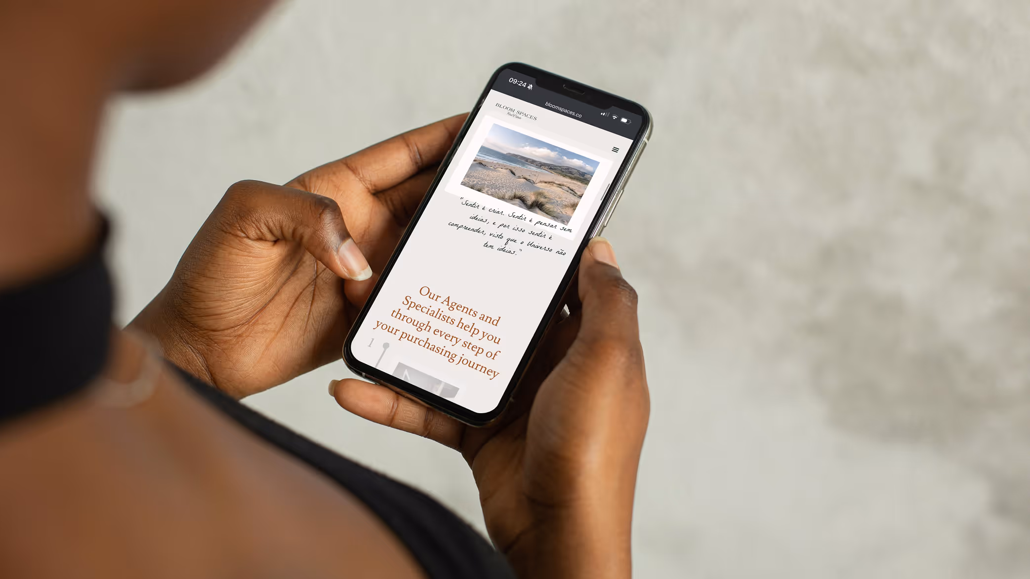 Person holding a smartphone displaying Bloom Spaces website with text about agents helping through purchasing journey.