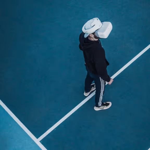 Person wearing a virtual reality headset standing on a blue court with white lines, viewed from above.