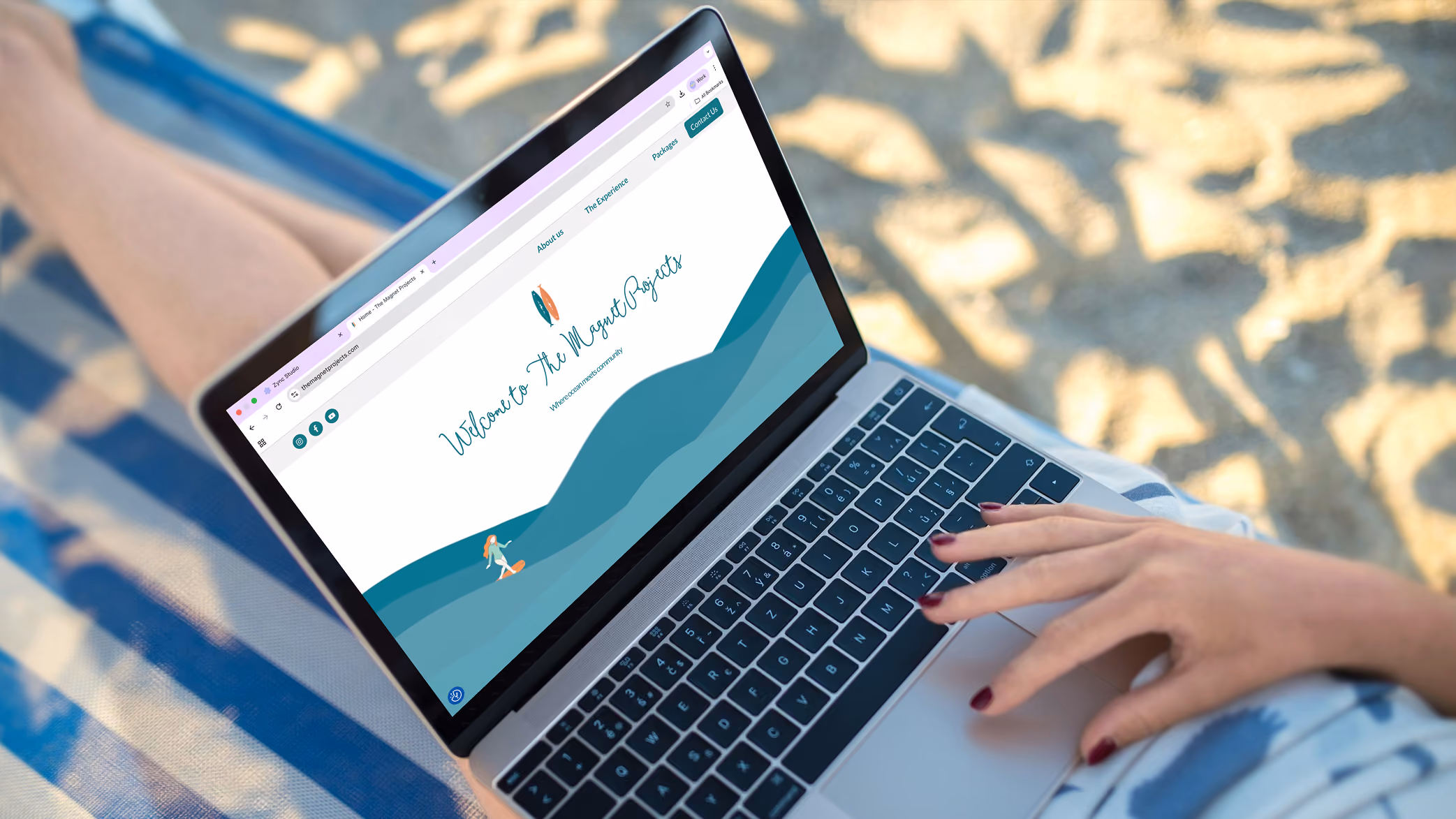 Person using a laptop on a beach chair with a website titled 'Welcome to The Magnet Projects' on the screen.