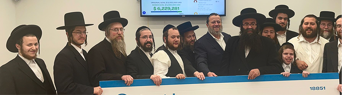 Group of men in formal attire and hats holding a large check, standing indoors.