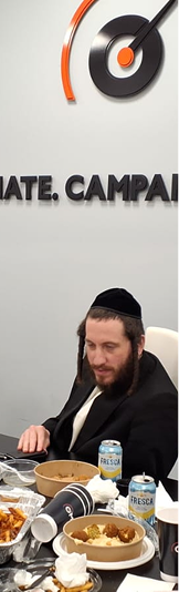Bearded man in traditional Jewish attire sitting at a table with food and Fresca cans.