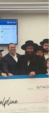Group of men including two with traditional black hats and beards standing behind a large check dated 9/14/23.