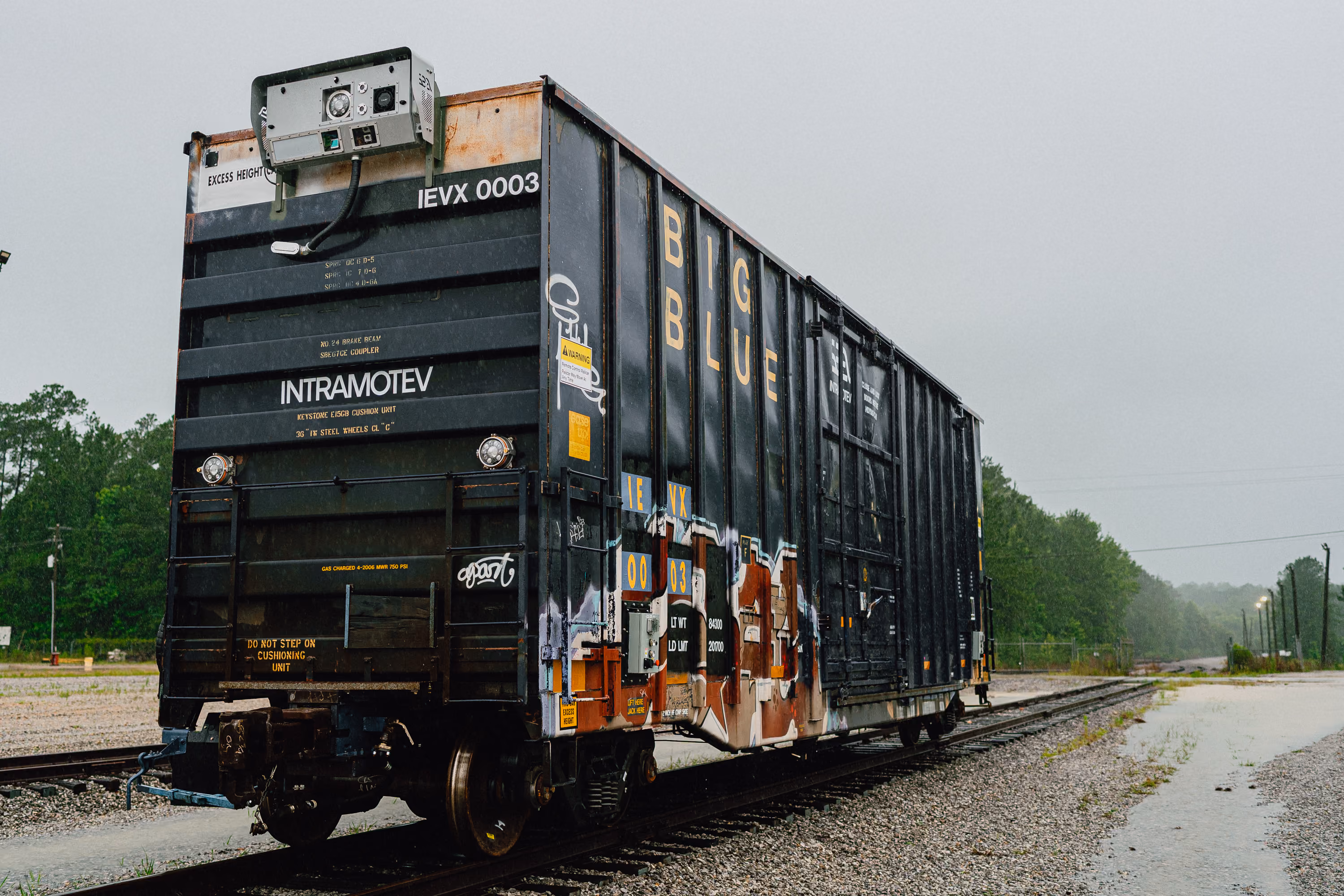 Black railroad freight car with graffiti and the words INTRAMOTEV and BIG BLUE on tracks.