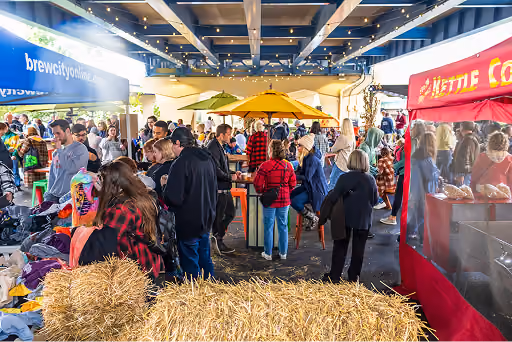 People walking around a barn with hay bails, merchant stalls, and food