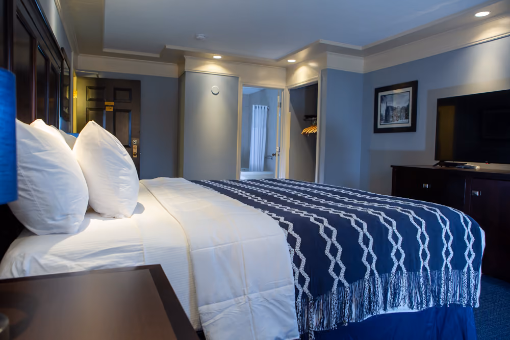 King Jacuzzi guest room with white bedding, navy patterned throw, television and bathroom visible from the bed