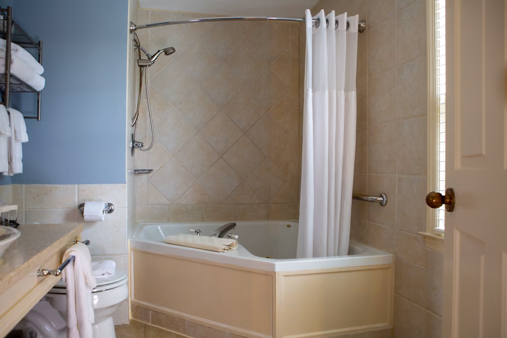 Private bathroom with large corner Jacuzzi tub, tiled surround, shower fixture and white curtain