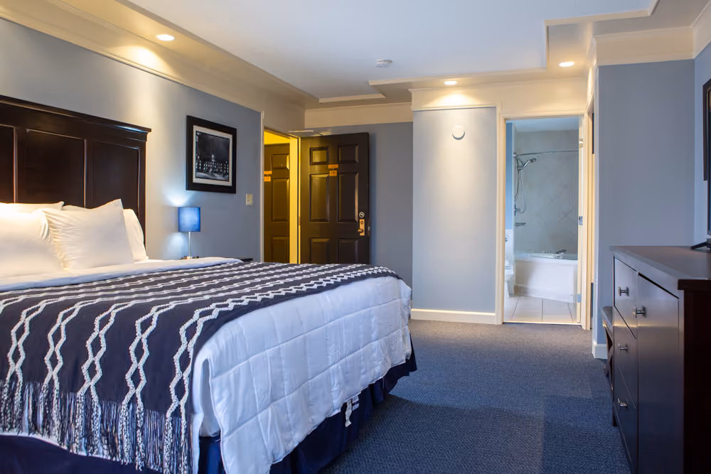 King Jacuzzi guest room with white bedding, navy throw and open doorway leading to the private bathroom
