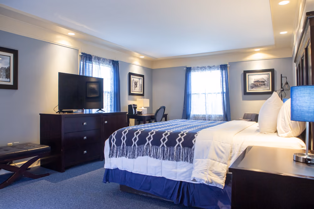 Wide view of king Jacuzzi guest room with white bedding, navy throw, television, desk and seating area