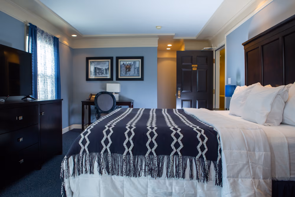 King guest room with white bedding, navy patterned throw, desk, television and blue-accented decor