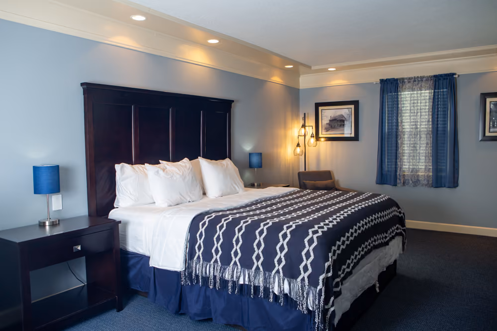 Spacious king guest room with dark wood headboard, white bedding, navy throw, seating area and large window